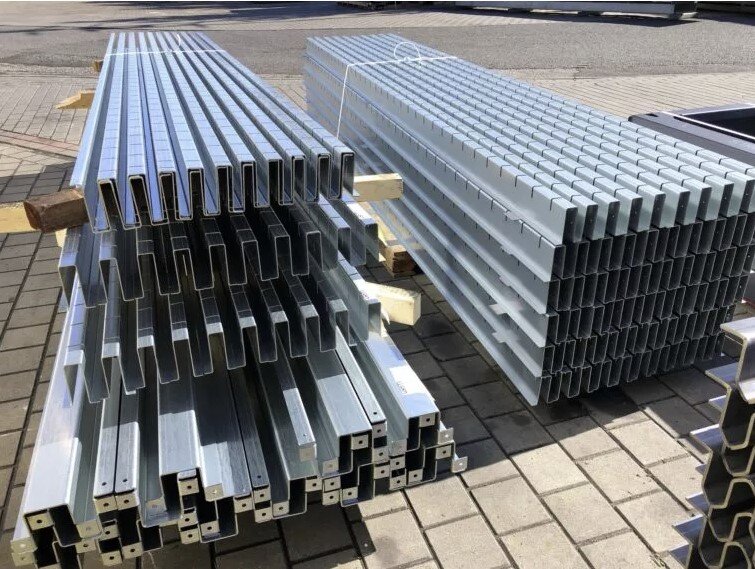 Stacks of galvanized steel C-channels neatly arranged on wooden pallets outdoors. The image shows uniform cold-formed profiles prepared for storage or transport in an industrial setting.
