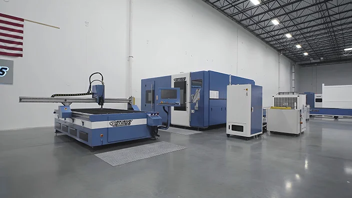 Modern production hall with Otinus CNC machines, including a fiber laser cutting system and enclosed processing units, arranged in a clean, well-lit industrial space with polished concrete flooring.