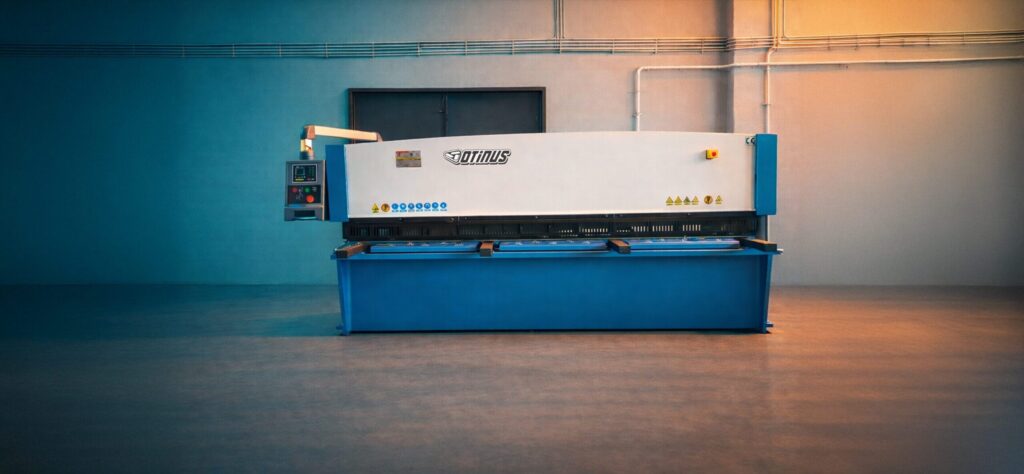 Front view of the Otinus Base guillotine shear in an industrial hall, emphasizing its symmetrical, solid construction, precise cutting mechanism, and clearly arranged control panel designed for efficient operation.