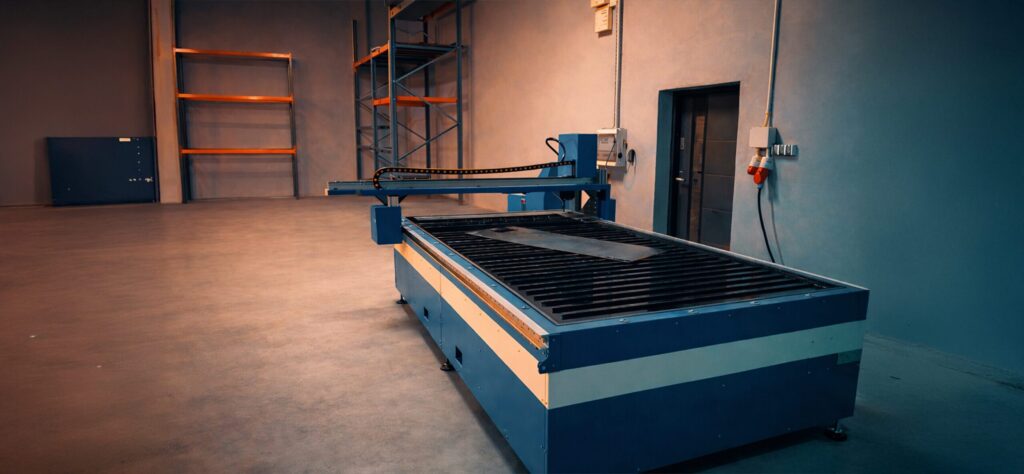 Industrial CNC plasma cutting machine with a water table, prepared for precise sheet metal cutting and installed in an organized production hall with adjacent storage facilities.