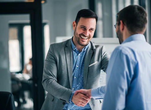 Two professionals in a modern office shake hands with a smile, symbolizing a successful partnership and the completion of a favorable financing agreement.